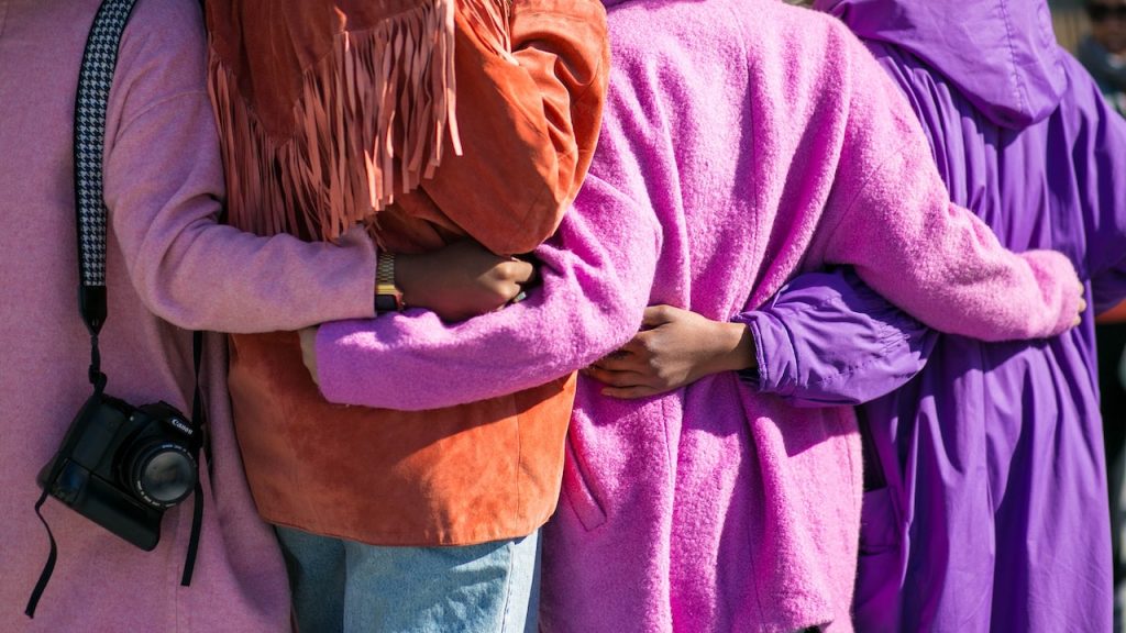 The backs of four women all with their arms around each other's waists.