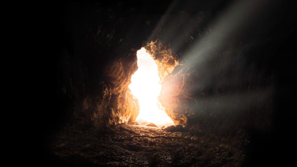 Daylight streaming through a rocky entrance into a dark cave.