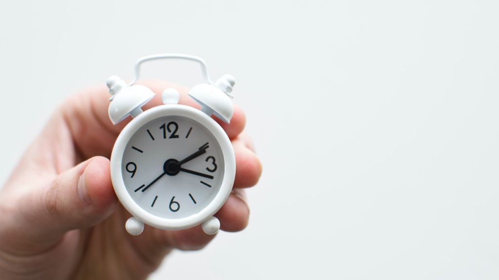 A hand holding a tiny alarm clock.