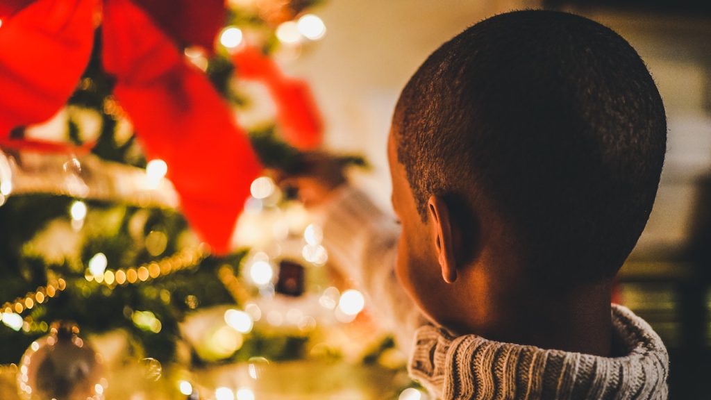 A boy reaching out and touching an illuminated Christmas tree.