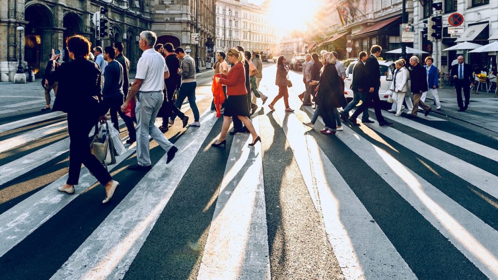 A cross walk in a city, at early morning, with crowds of people crossing.