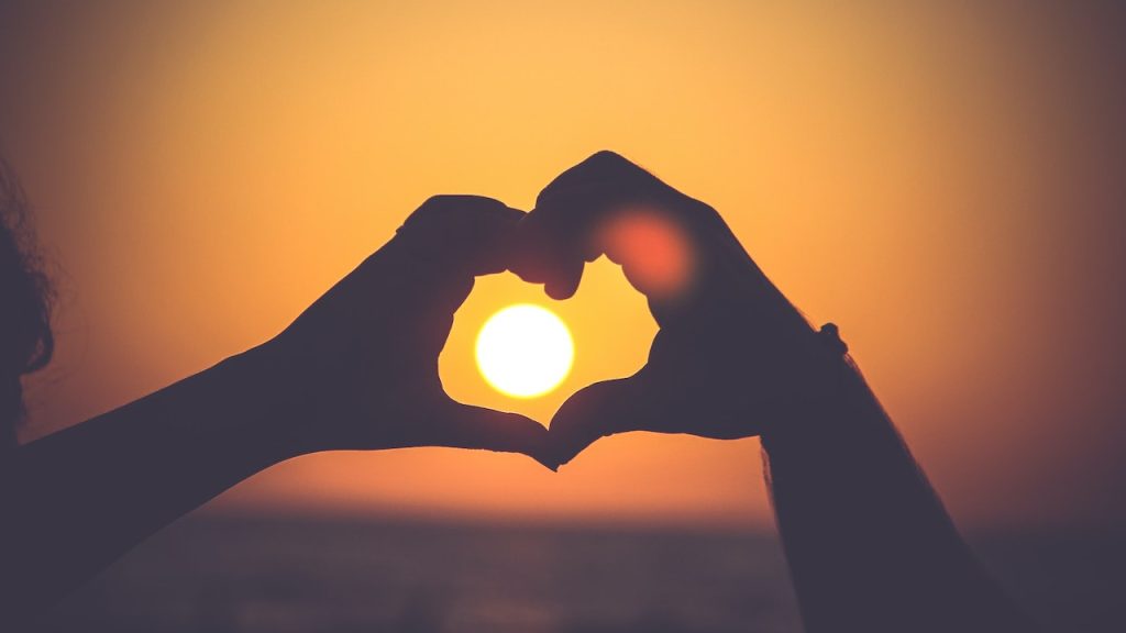 A silhouette of two hands making a heart shape with a sunset in the background.