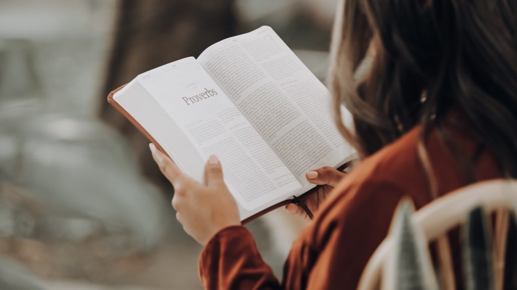 A woman sitting in a chair reading an open Bible.