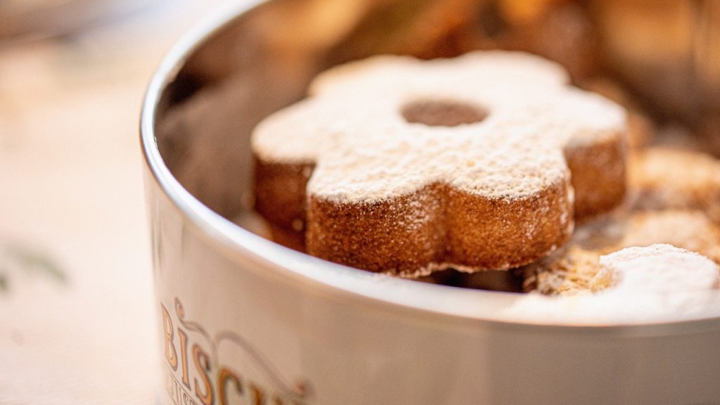 A shortbread cookie dusted with icing sugar sitting at the top of a biscuit tin.