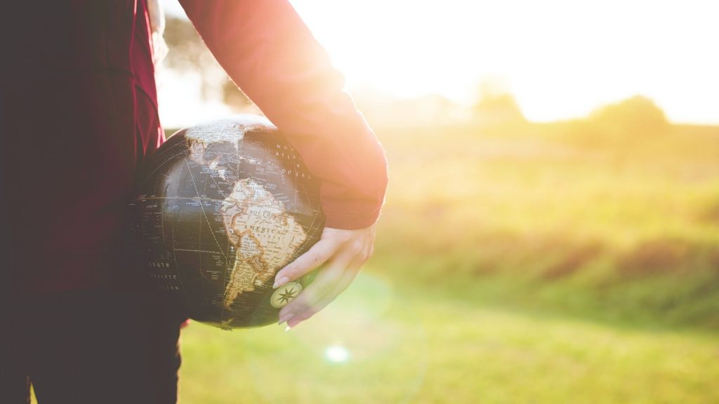 A woman holding a beach ball under her arm with a pattern of the world on it.