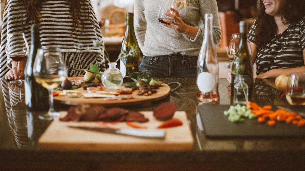 People standing at a counter holding glasses of wine with platters of meats and vegetables on the counter.