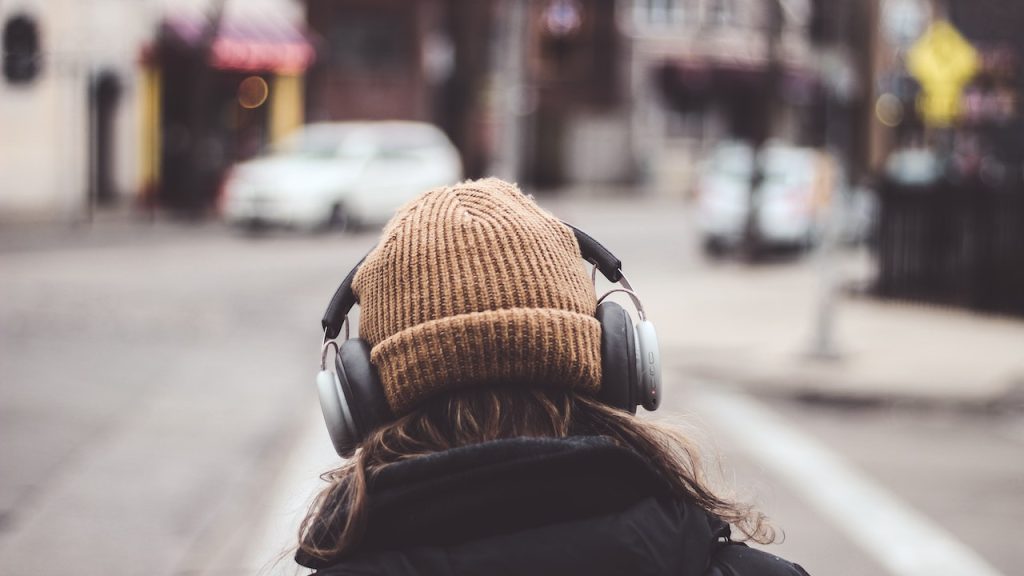 The back of a person in an urban street wearing a beanie and headphones.