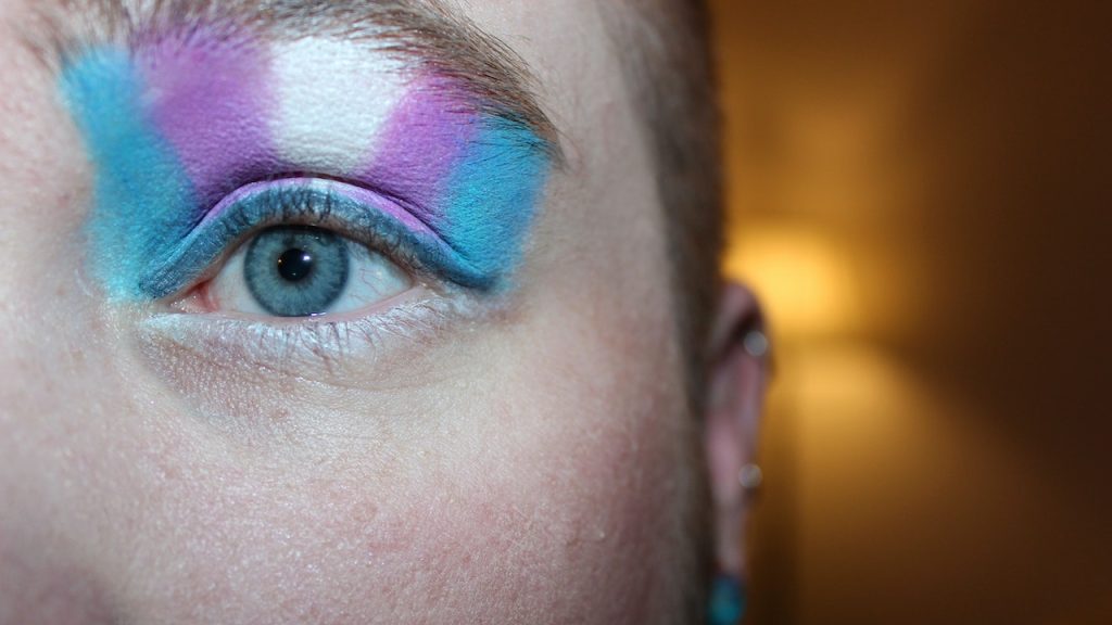 A closeup of thick stripes of eye shadow over an eye in the trans colours of blue, purple, and white.