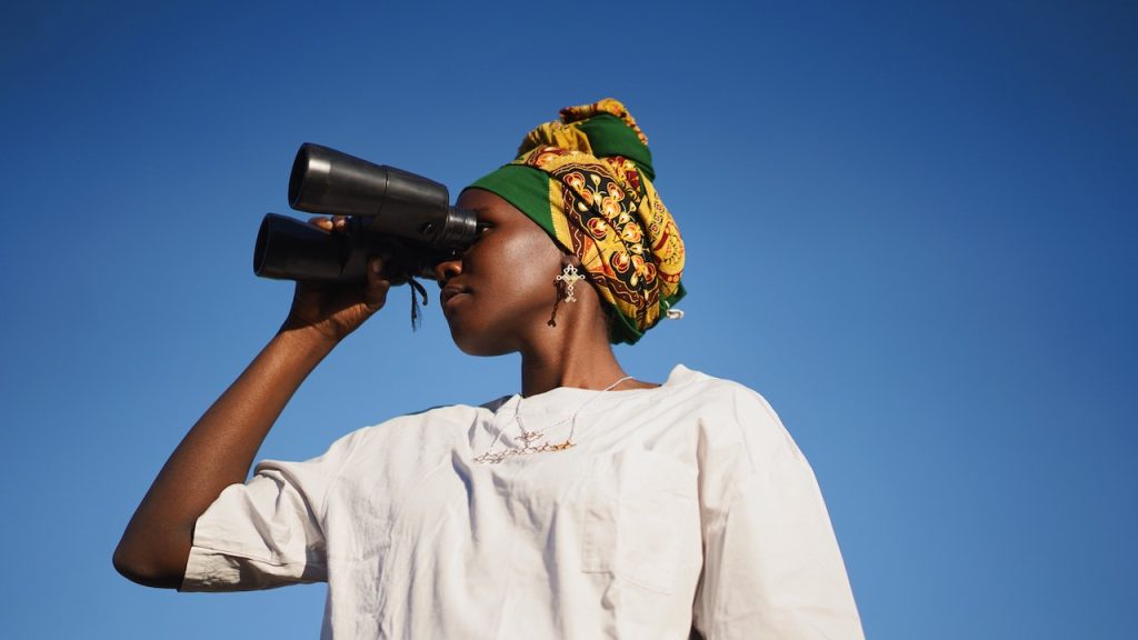 A woman wearing a kaftan looking through a pair of binoculars.