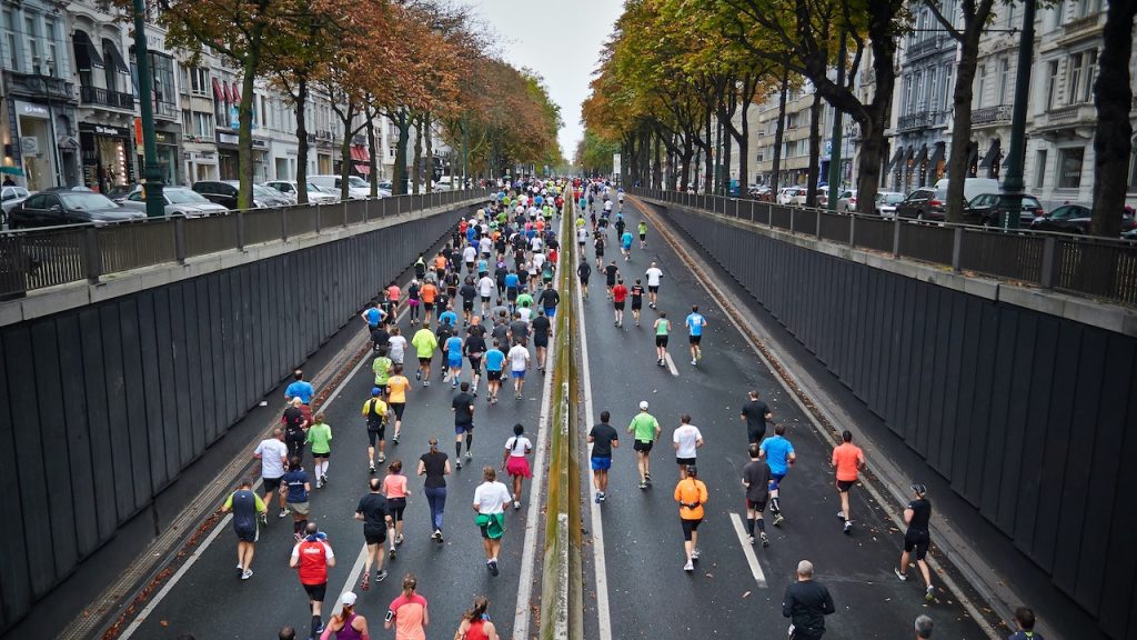 Marathon runners running under an underpass in a cityscape.