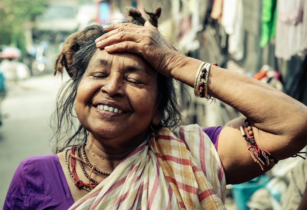 An Indian woman smiling and looking relieved and contented with her hand on her forehead.