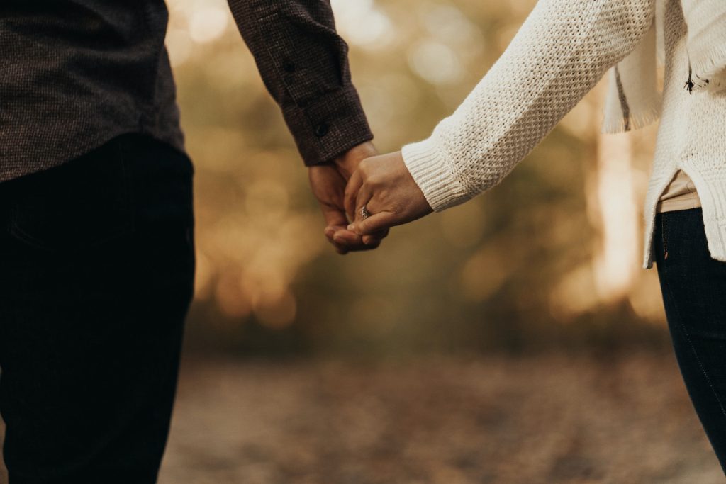 A couple walking in woodland holding hands but standing quite far apart.