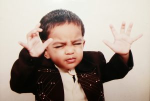 A boy with his eyes tight shut in concentration holding his hands palm up as if praying or blessing someone.