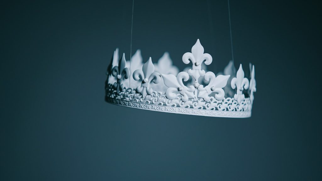 A delicate white crown being suspended from wires and artfully lit in a studio.