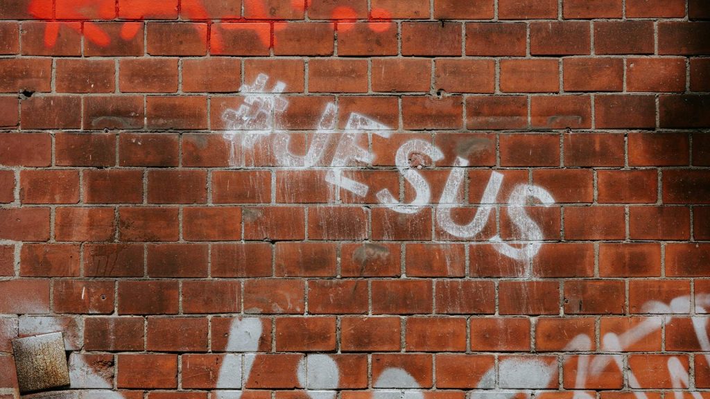 The word Jesus stencilled on a brick wall.