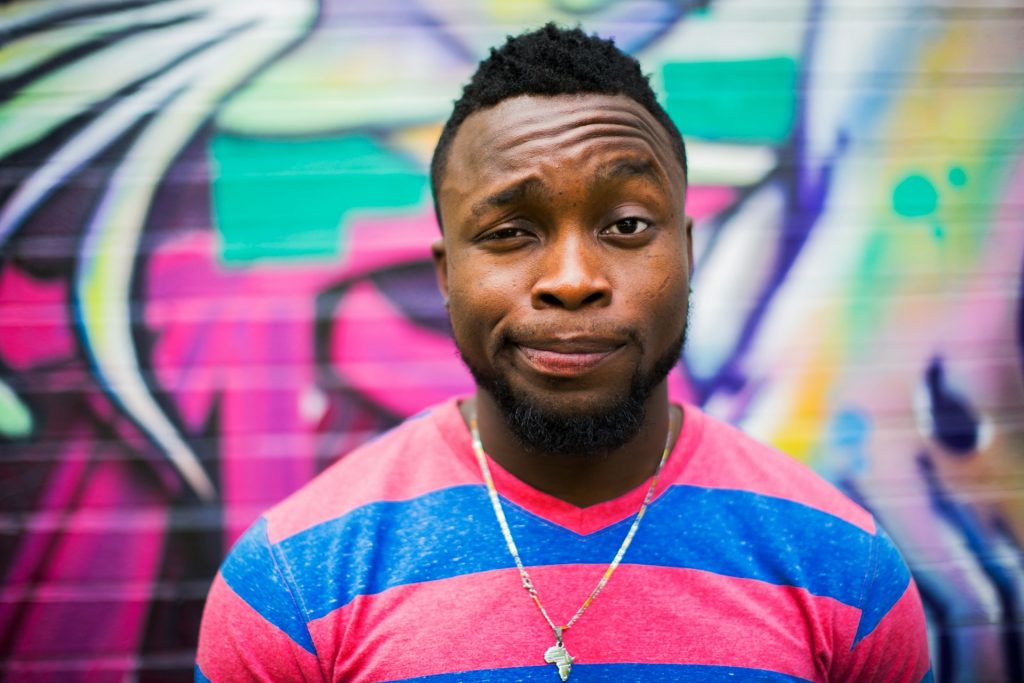 A trendy African man winking standing before a graffiti wall.