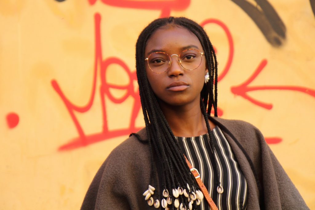 A proud young woman with dreadlocks standing in front of an urban graffiti wall.