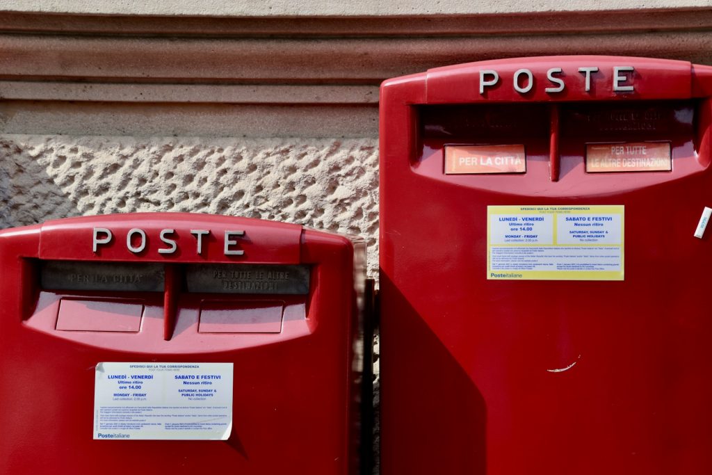 Two red post boxes stand side by side. One is slightly taller than the other and both have the words 'POSTE' written above the letter slots.