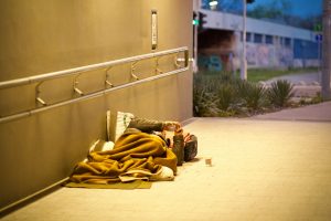A homeless person lies under a blanket in an urban underpass.