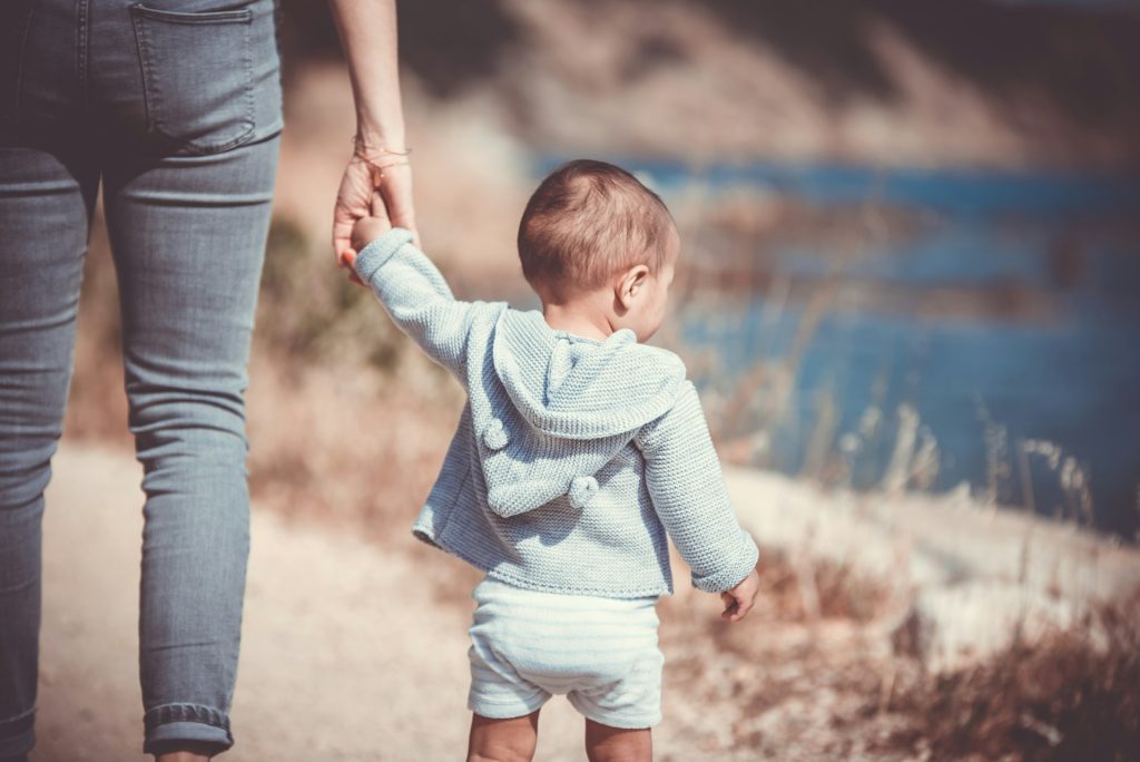 A toddler going for a walk holding the hand of a parent.