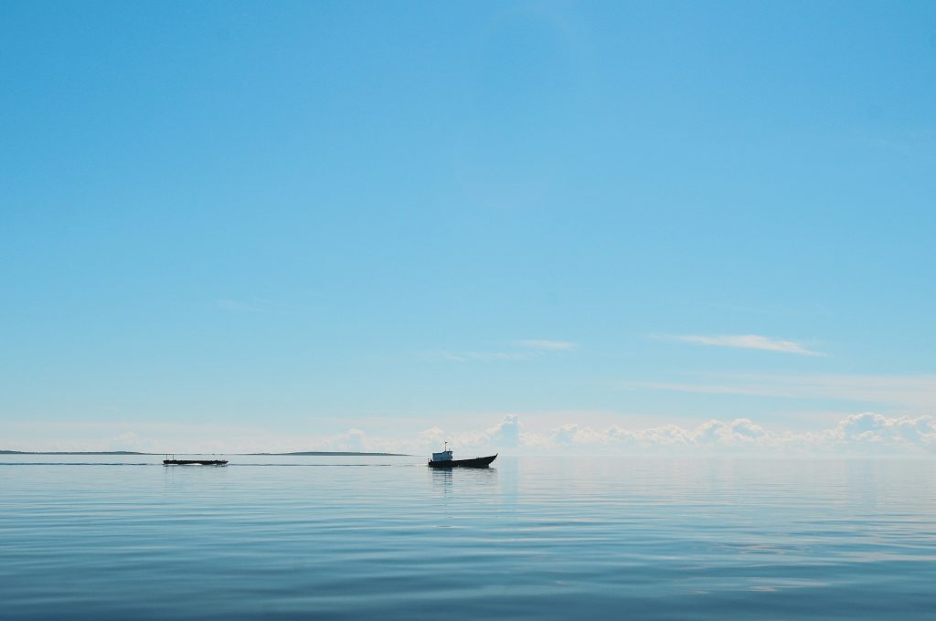 Trust A boat, out on a lake sits in a calm sea under a blue sky.