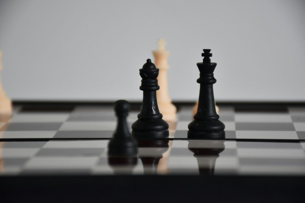 Pieces on a chess board. The white king, alone, faces three black pieces.