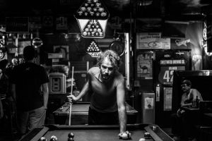 An unkempt man plays pool in a dive bar.