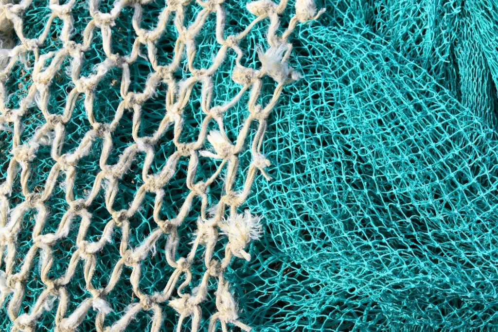 A closeup of two fishing nets. One white with large holes and one turquoise with small holes. The white one is overlaid over the greeny blue one.