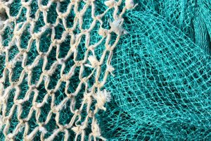 A closeup of two fishing nets. One white with large holes and one turquoise with small holes. The white one is overlaid over the greeny blue one.