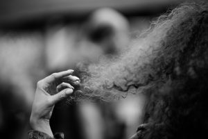 A woman stands, holding strands of her hair between her fingers.