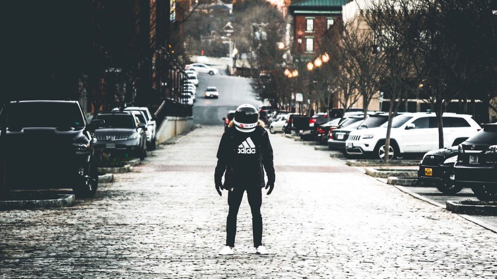 A person wearing a crash helmet, looking a bit like a space man, standing in the middle of an empty road in a city.