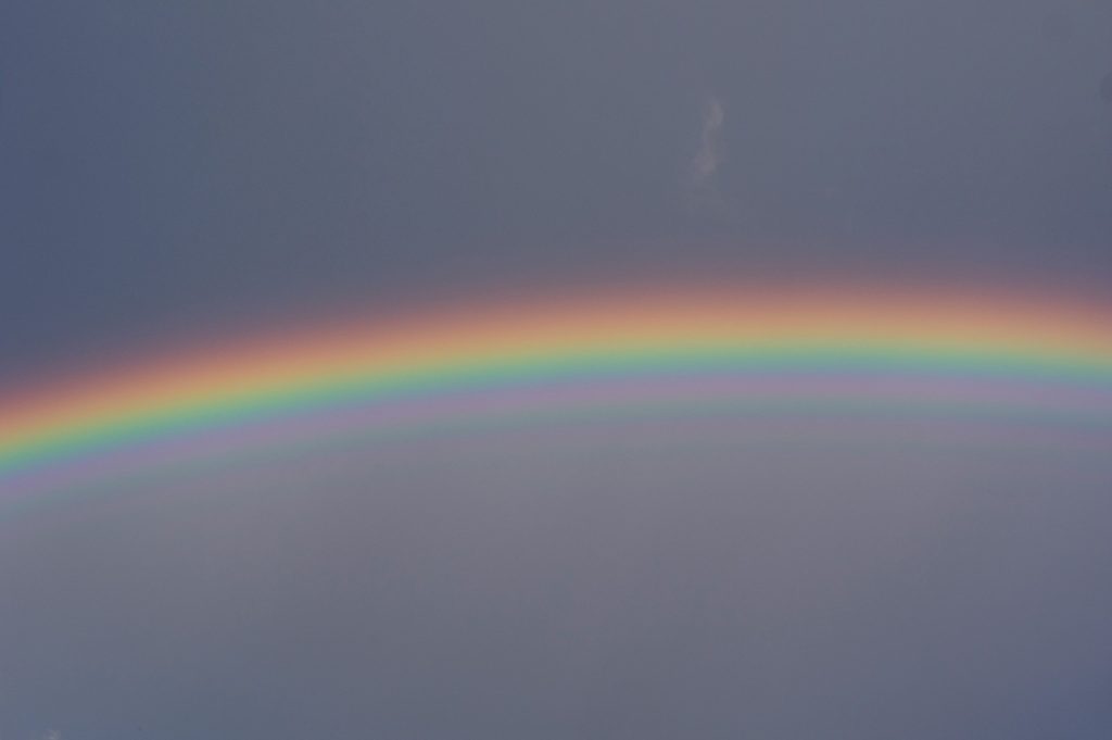 A rainbow streaks across a dull blue sky.