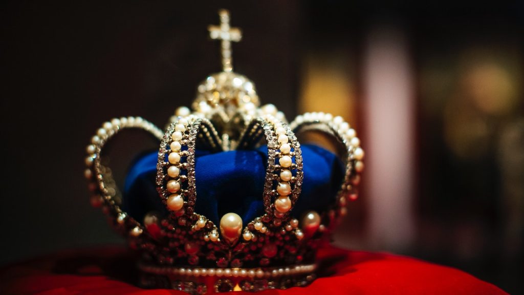 An expensive looking bejewelled crown sitting on a plush cushion.