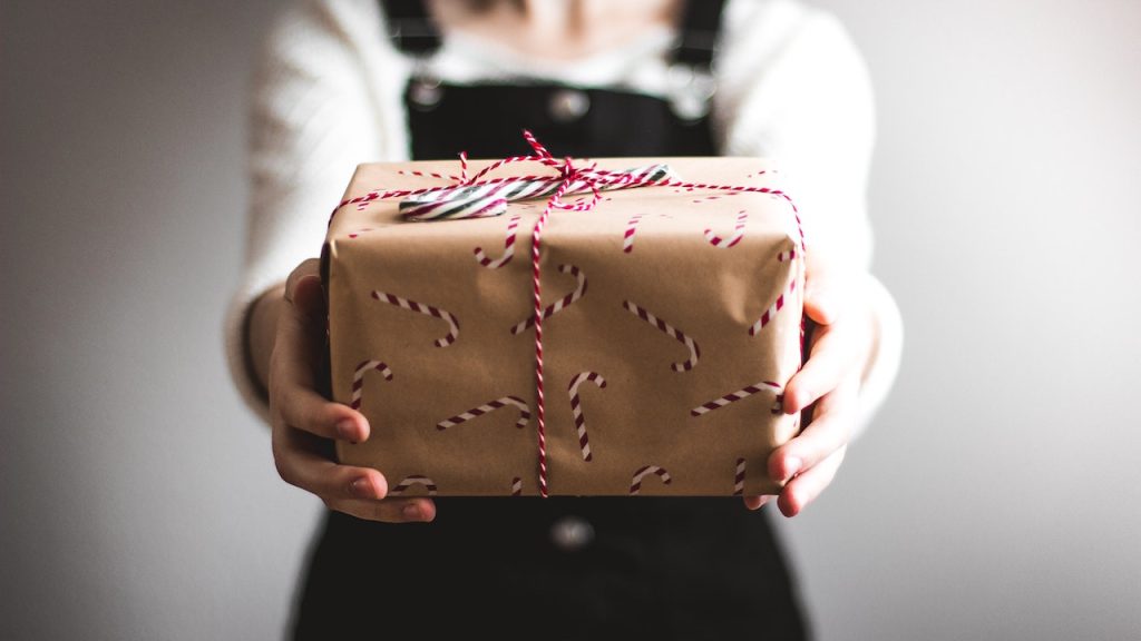 A person holding a large string-wrapped parcel towards the camera. The parcel has a pattern of candy canes all over it.