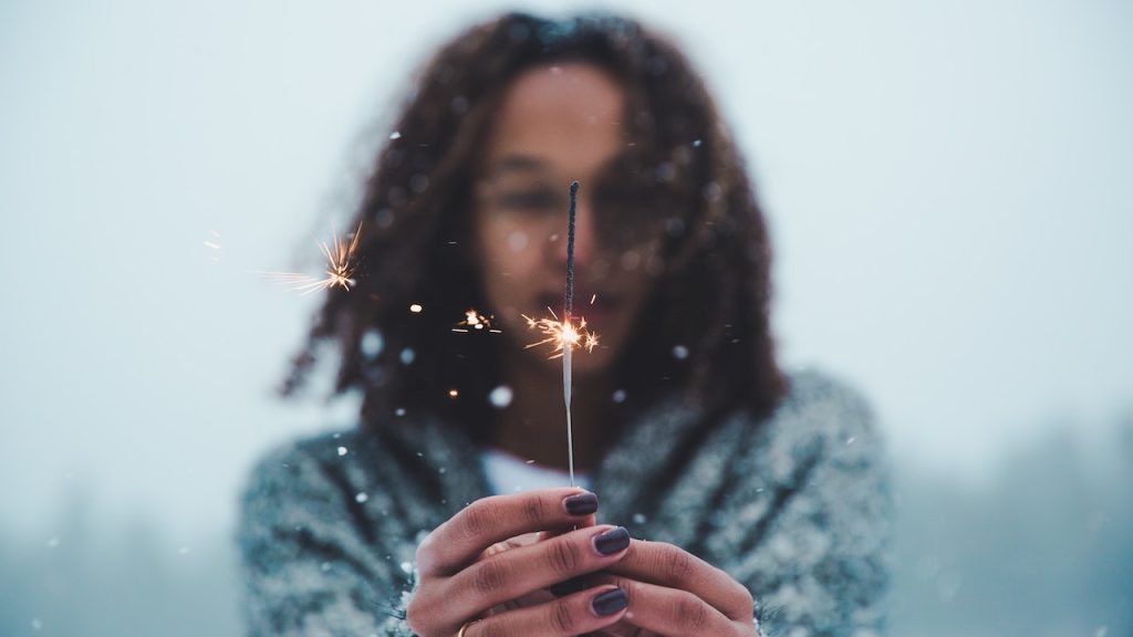 A woman looking in wonder as she holds a lit sparkler in front of her