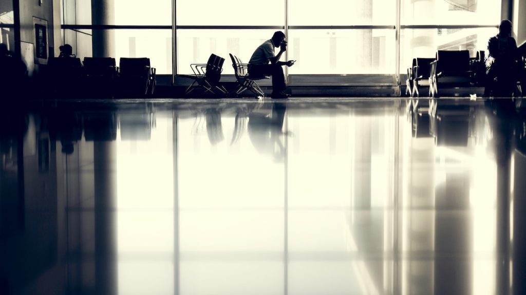 A silhouette of man sitting alone in an airport lounge.