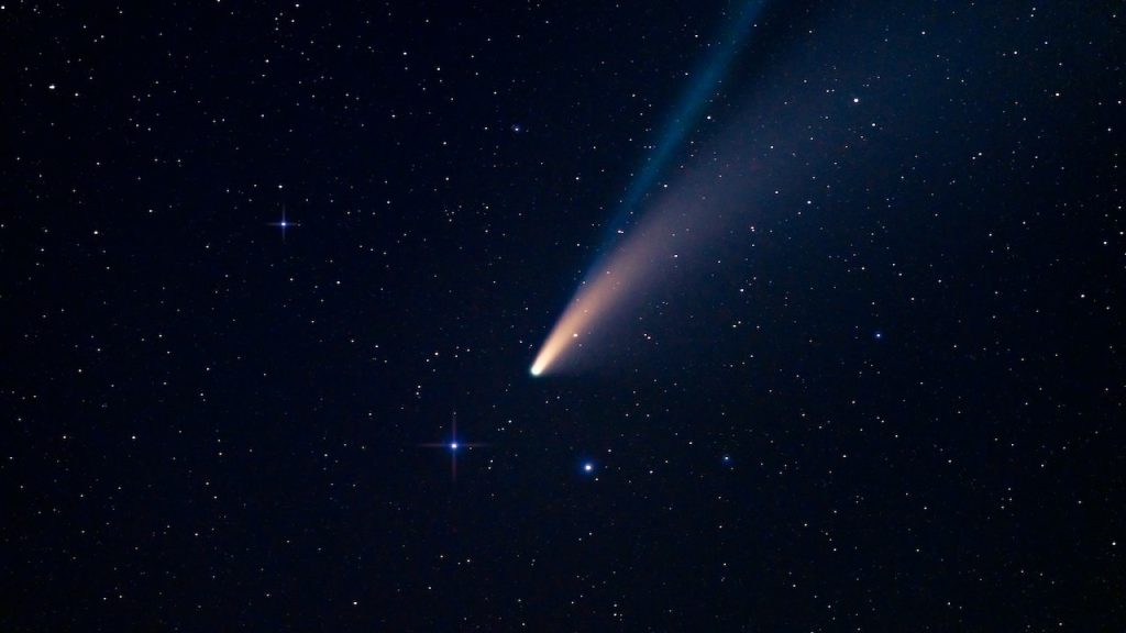 A comet streaming across a night sky with a long glowing tail.