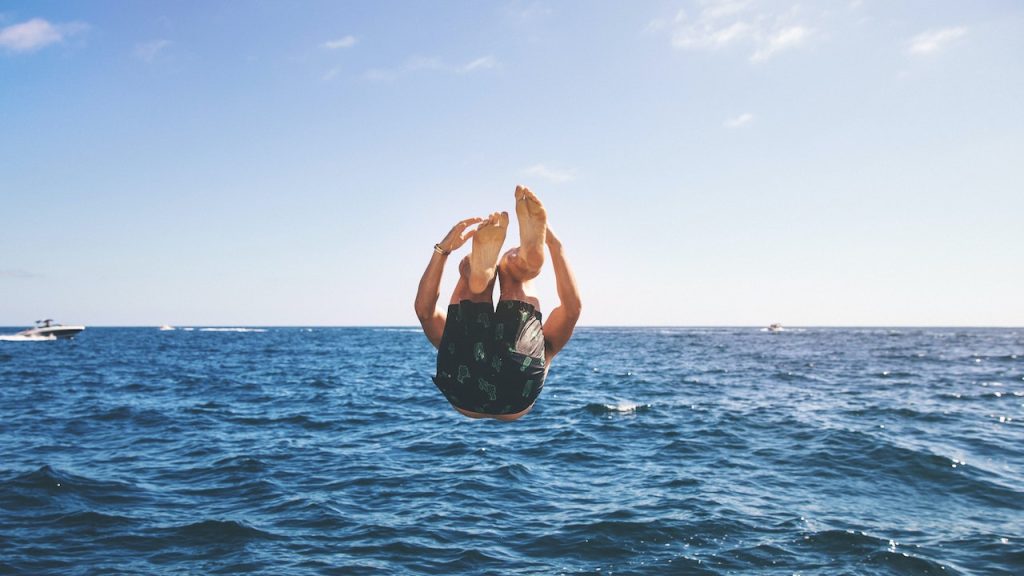 A boy mid-air doing a backflip into an ocean.