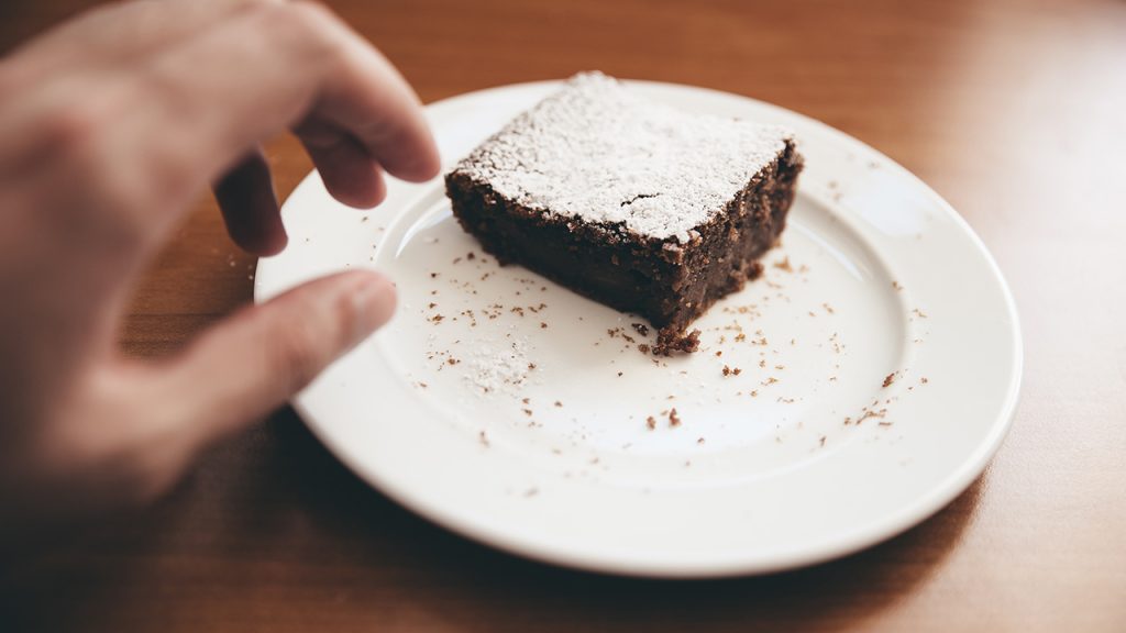 A hand reaching out for a last chocolate brownie sitting on a plate.