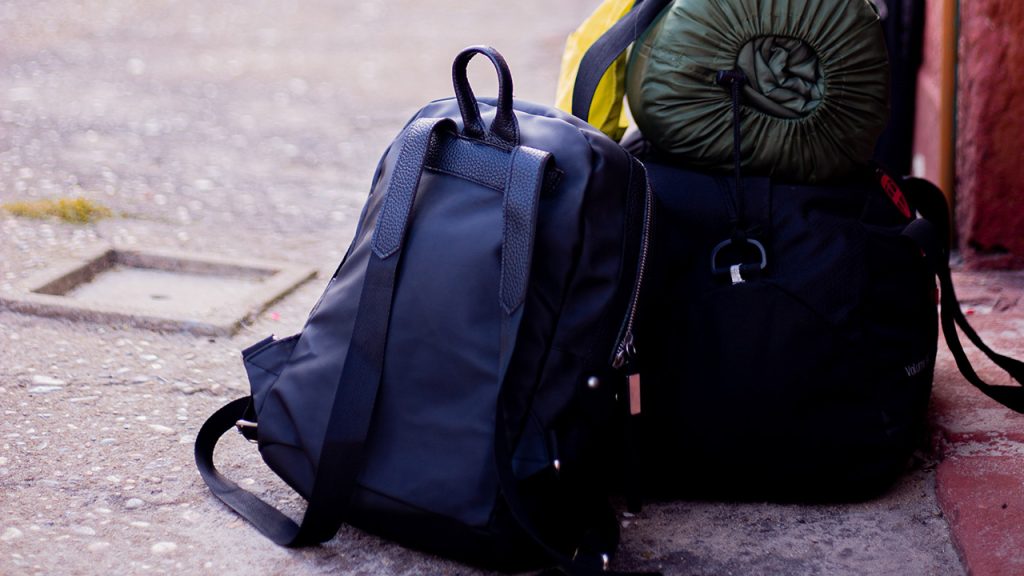 Bags set on a street with a backpack and sleeping bag and other assorted baggage.