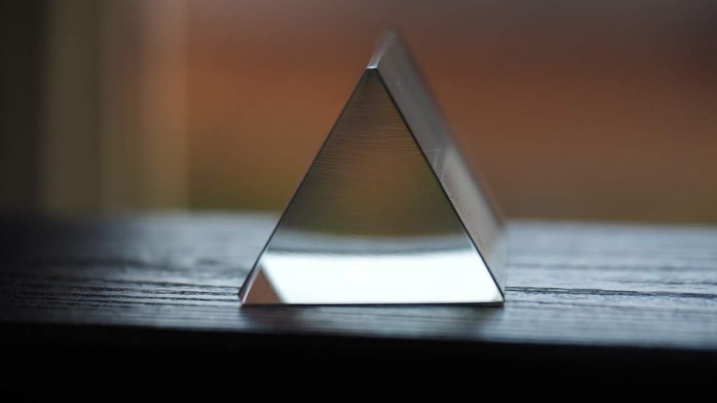 A glass prism standing on a wooden shelf.