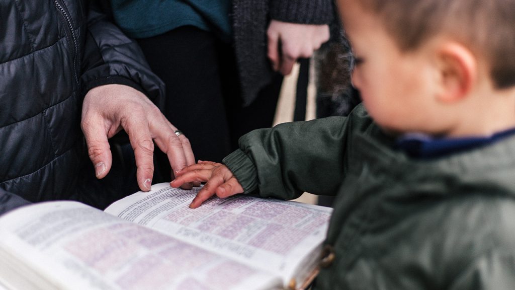 A young boy pointing to a passage in a Bible and showing an adult.