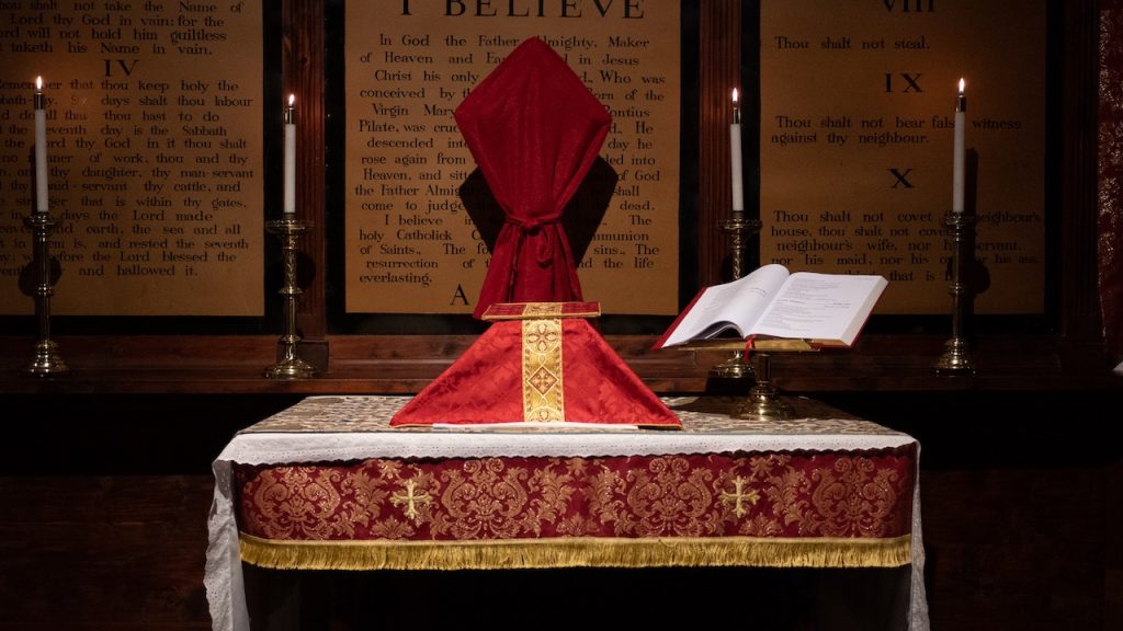 A highly decorated communion table set for Lent with a cross covered in a cloth, candles, and an open Bible on a brass stand.