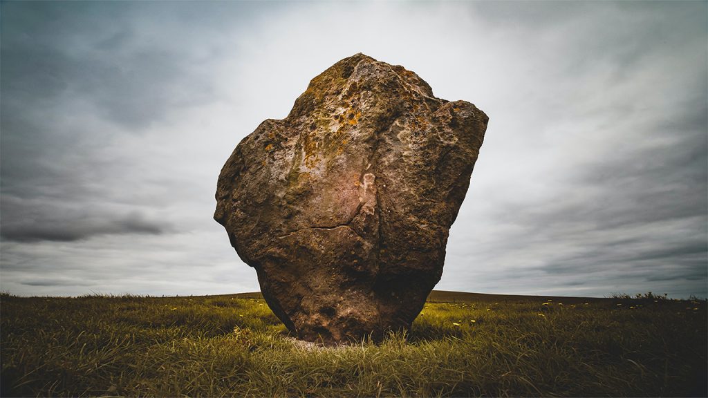 A large standing stone or rock in a grassy highland field.