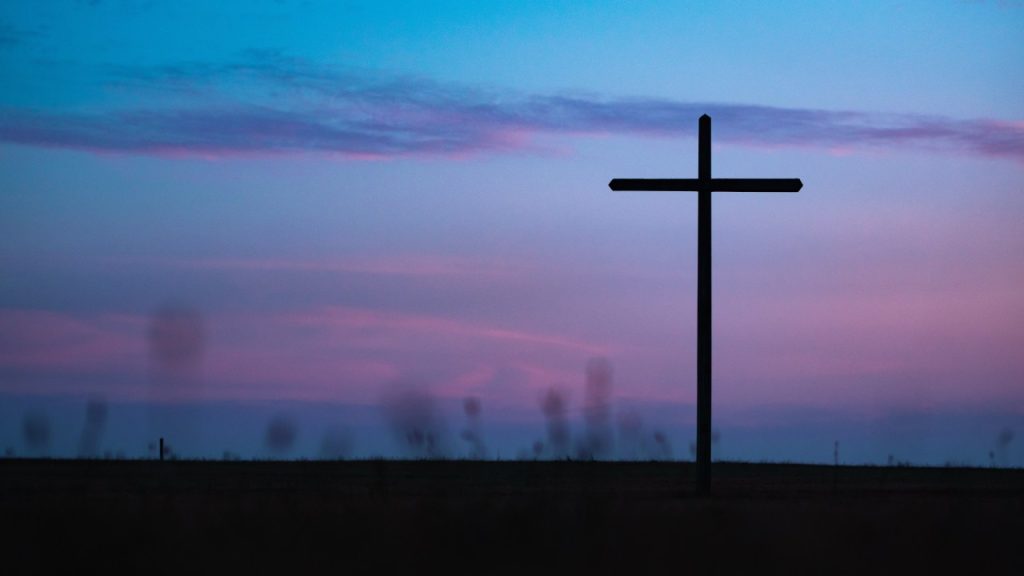 A simple wooden cross standing in a field at dusk.