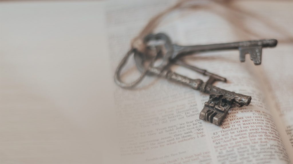 Three very old iron keys tied together with string lying on an open Bible.