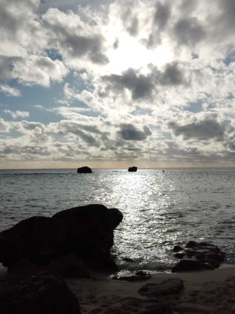 A beach with huge boulders, the sea, and a cloudy sky.