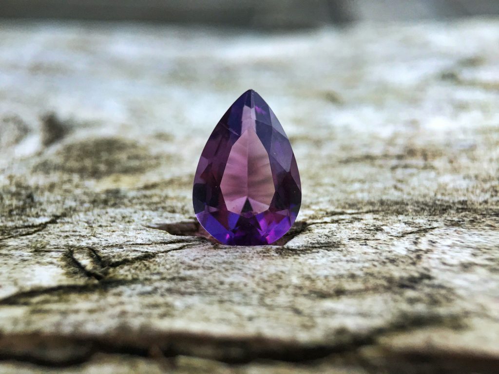 A large purple cut gemstone sitting on a rock.