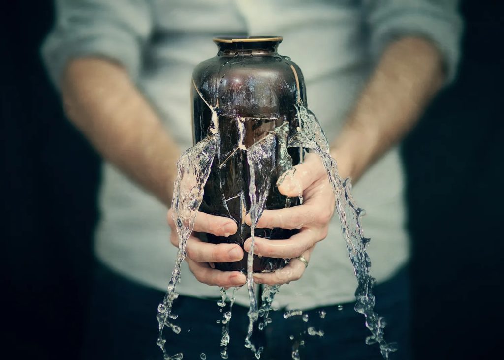 A man holding a cracked pot which is leaking water.