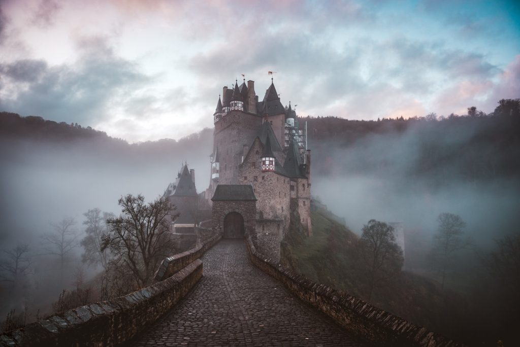 A German turreted castle on a mount in a thick fog-filled forest.